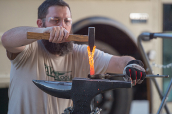 Mike Martin, a Mennonite pastor turned blacksmith from Colorado Springs, forms the metal of what used to be a gun into a hand-held garden tool at the Hesston College beating guns event. — Larry Bartel/Hesston College
