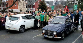 A group from East Chestnut Street Mennonite Church celebrates the charging stations going live. In the foreground is Brandon Hol­linger’s 1968 Saab, converted to electric power. — East Chestnut Street Mennonite Church