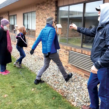 Wanda Reinford Martin, Emilia Reinford Martin and Terry Reinford Martin sing near Karen Davidson’s window at Courtyard Healthcare in Goshen, Ind., while Bruce Miller, right, holds a phone for Davidson to be able to hear. — Teresa Dutchersmith