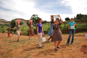 During an interterm in Lesotho and South Africa that included home stays, Bethel College students try their hand (or their heads) at balancing and carrying water the way the village women did. Bethel College photo.