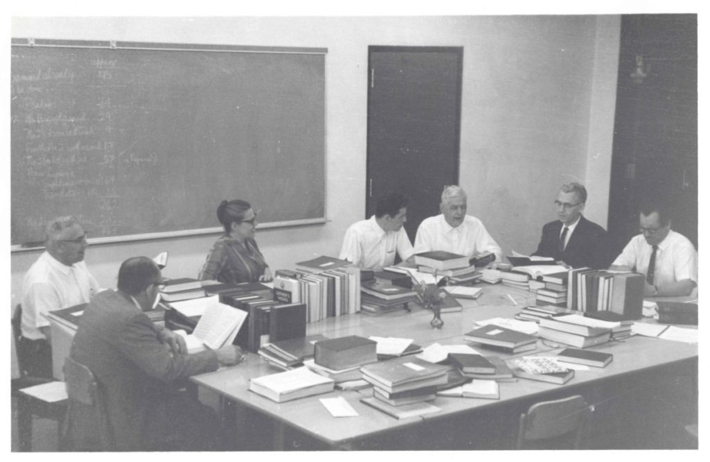 A meeting of the Joint Worship and Hymnal Committee. This committee produced the 1969 Mennonite Hymnal, with Mary Oyer acting as Executive Secretary. Starting from bottom left, and moving clockwise around table: Ed Stoltzfus, Paul Erb, Mary Oyer, John Ruth, Chester Lehman, Marvin Dirks, and Walter Klaassen. ~1963-1967